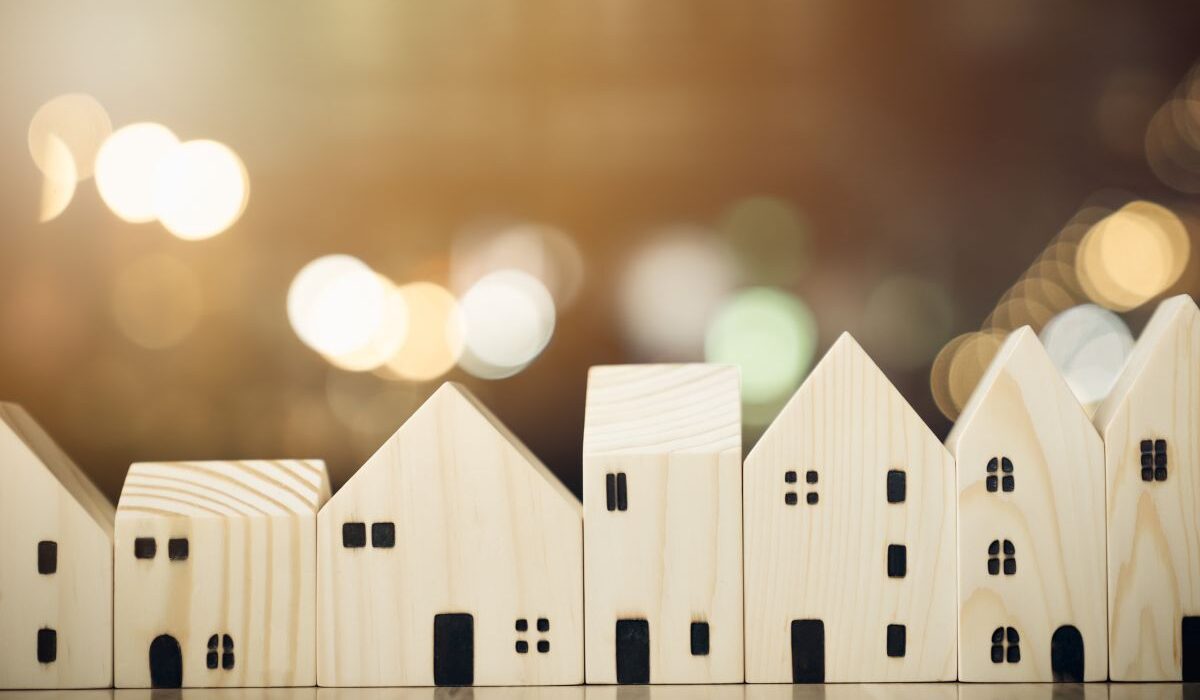 a row of small wooden models of houses in front of twinkling lights