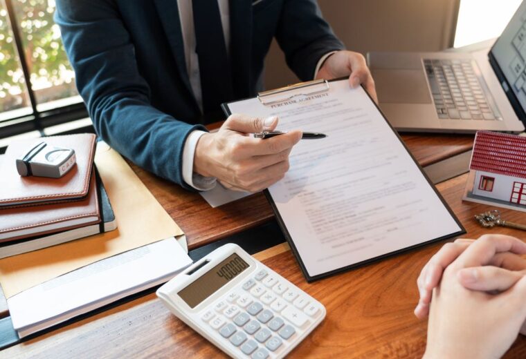 A man sitting at a desk with a laptop and calculator showing hte contents of a contract to a customer sitting opposite - Express Capital Financing