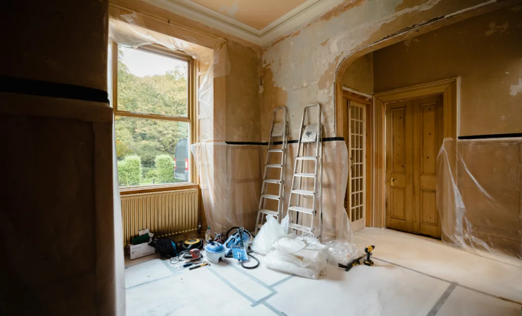 A room in a house undergoing renovation with a ladder, covered floors and tools lying nearby - Express Capital FInancing