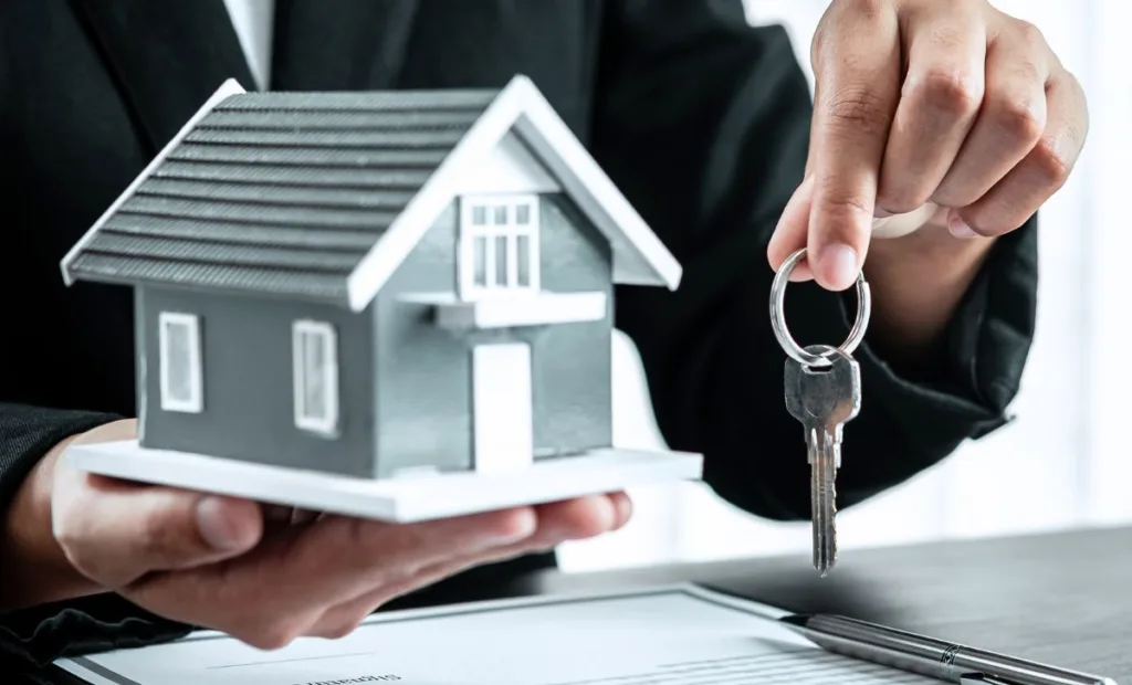A person in a suit holding a small house in one hand and a set of keys in the other - Express Capital Financing