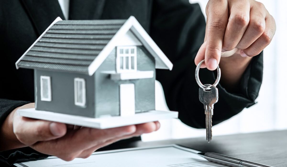 A person in a suit holding a small house in one hand and a set of keys in the other - Express Capital Financing