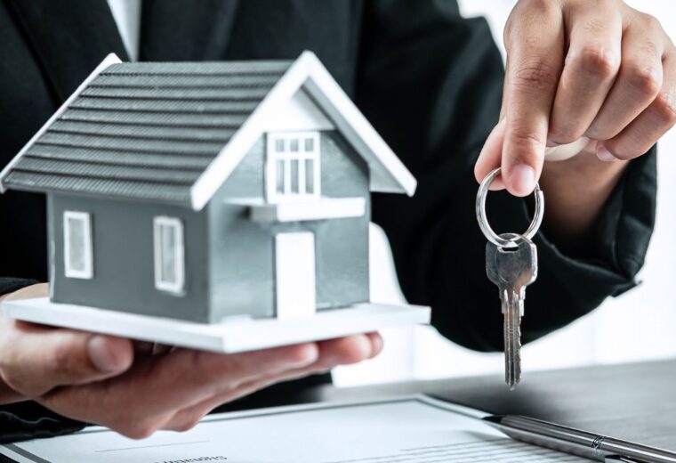 A person in a suit holding a small house in one hand and a set of keys in the other - Express Capital Financing