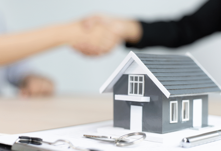 A small model of a house with keys in front of it ansd two people shaking hands in the background - Express Capital Financing