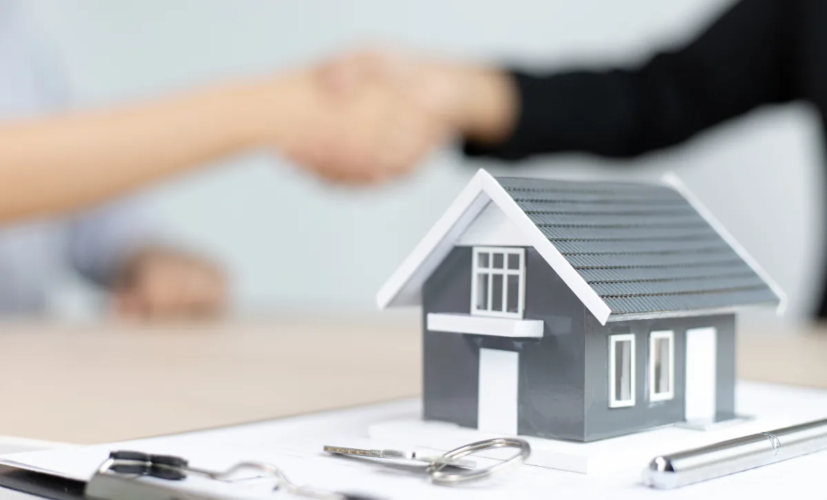 A small model of a house with keys in front of it ansd two people shaking hands in the background - Express Capital Financing