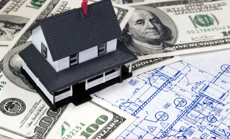 A small model house sitting on top of dollar bank notes - Express Capital Financing